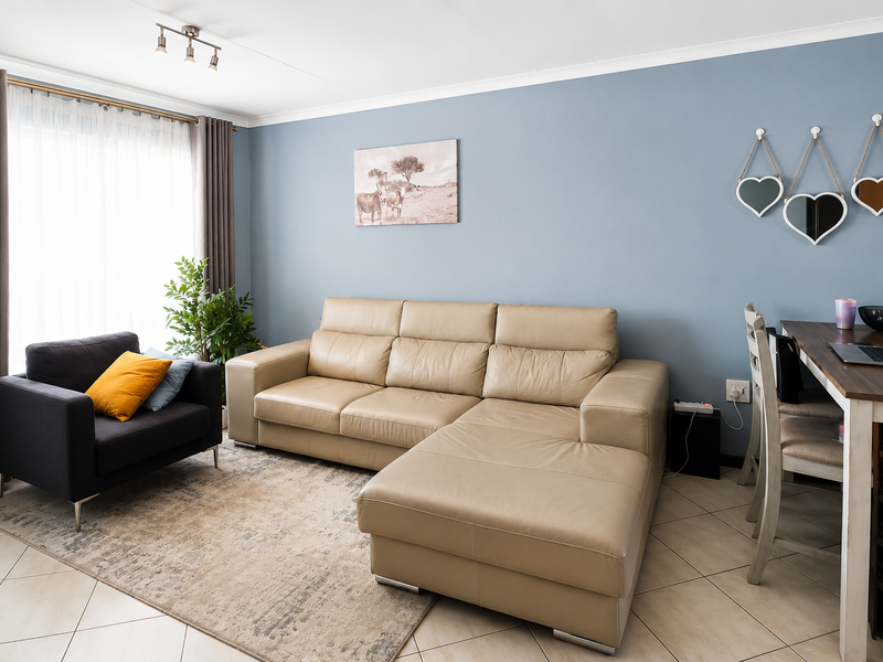 A well-maintained living room featuring neutral tiled flooring, soft blue accent walls, and ample natural light through large windows.