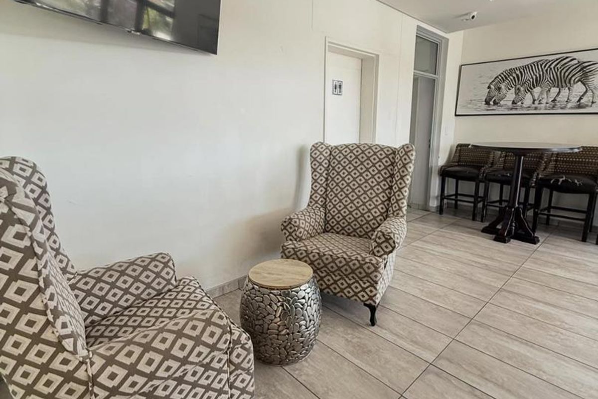A well-maintained hotel lounge area featuring large format floor tiles, recessed ceiling lighting, and a wall-mounted television.