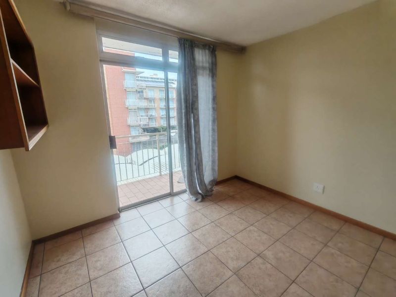 A vacant bedroom featuring tiled flooring, built-in shelving, and a sliding glass door providing direct access to a private balcony.