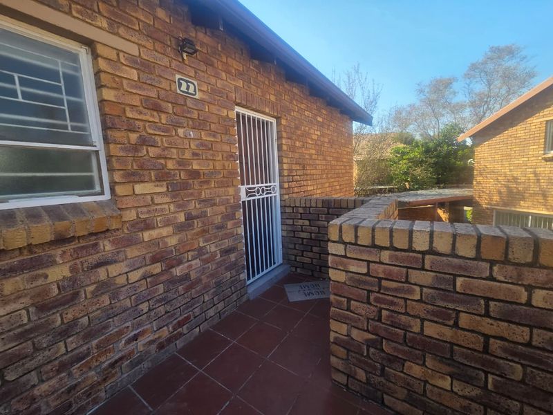 Exterior view of the apartment entrance featuring a face brick facade, tiled patio area, and secure gated access.