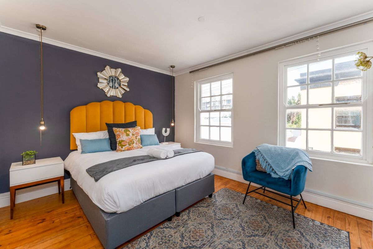 A well-maintained bedroom featuring polished timber flooring, sash windows, and a striking dark accent wall with integrated pendant lighting.