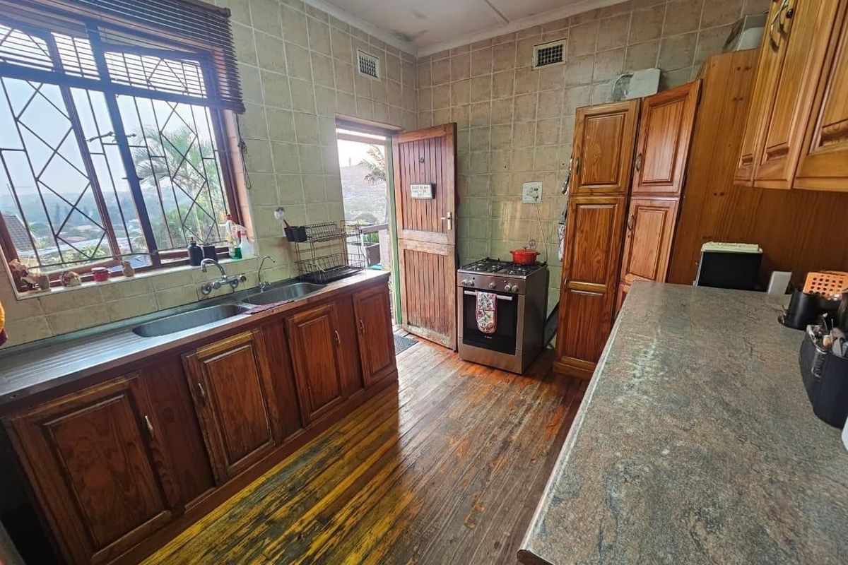 A functional kitchen featuring timber cabinetry, a double stainless steel sink, a freestanding gas stove, and tiled splashbacks with direct access to the exterior.