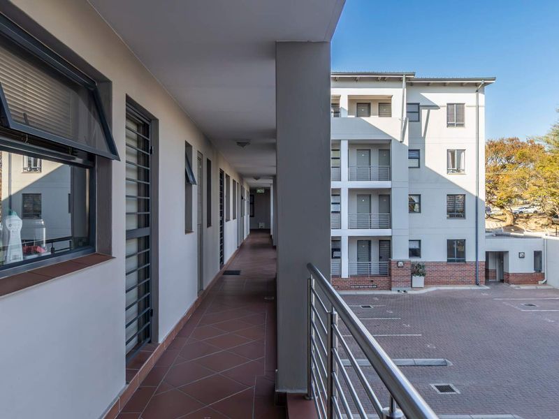 An exterior apartment hallway featuring tiled flooring, stainless steel balustrades, and security bars, overlooking a paved parking area.