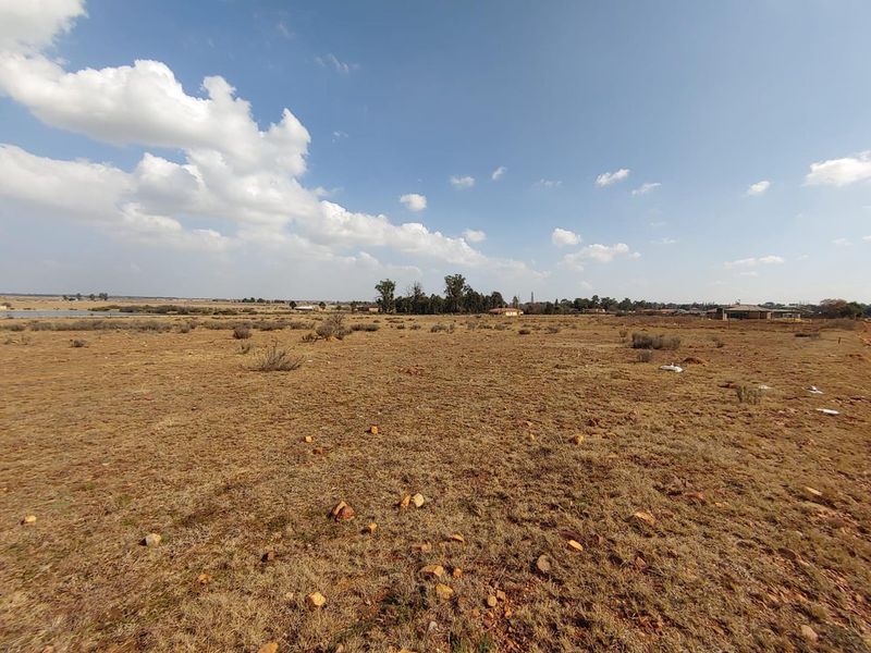 A wide-angle view of a vacant residential plot featuring natural dry grassland and distant horizon views.