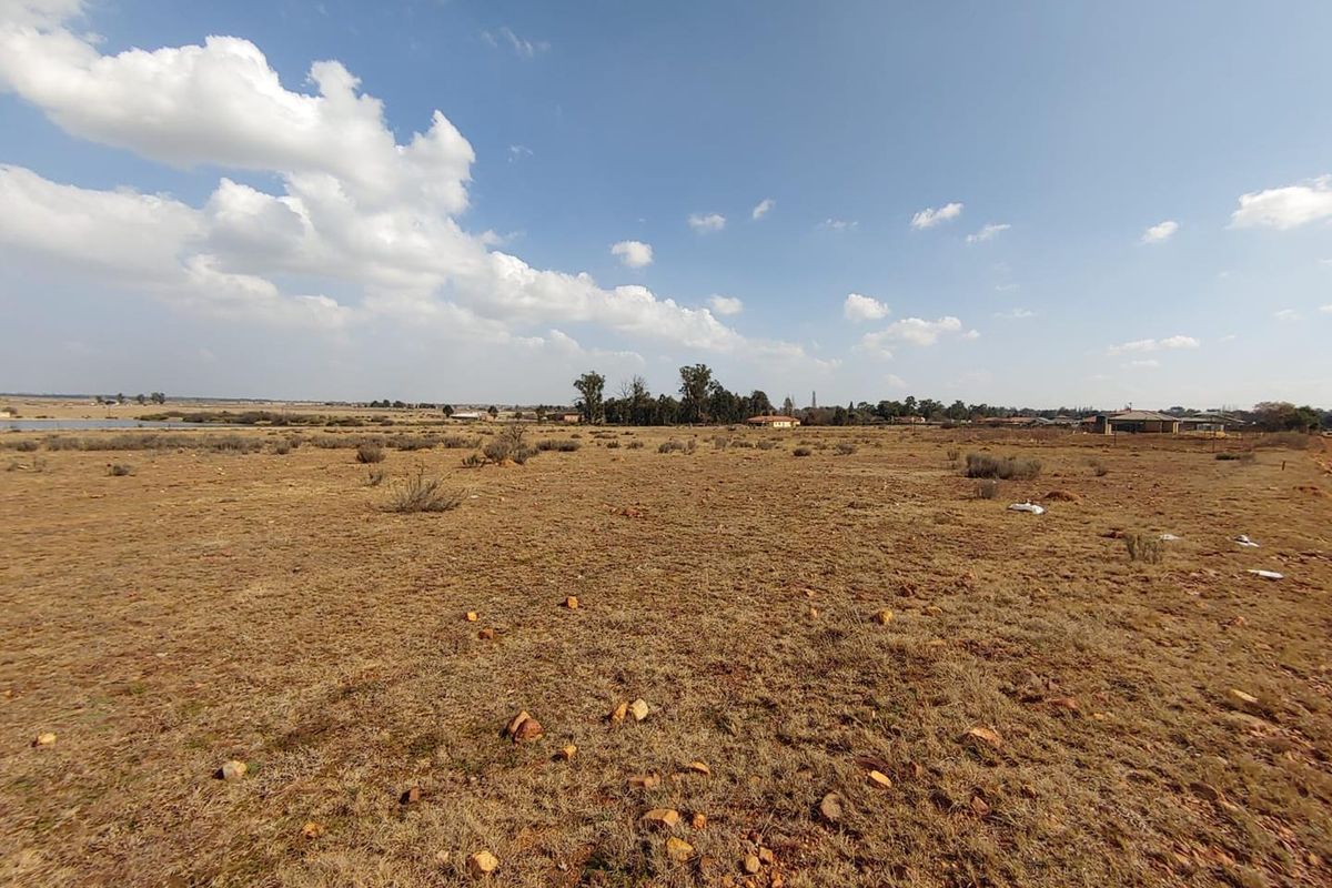 A wide-angle view of a vacant residential plot featuring natural dry grassland and distant horizon views.