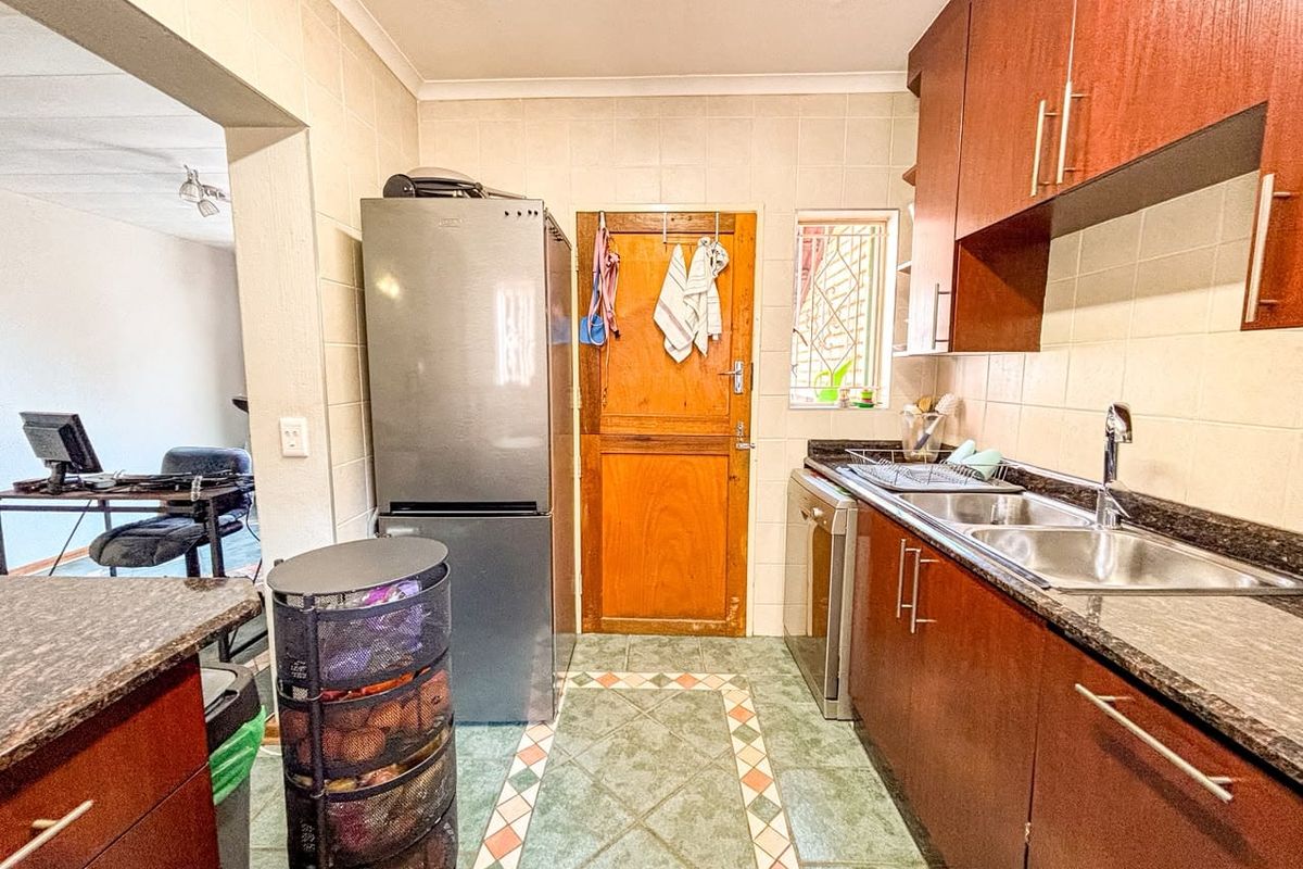 A functional kitchen featuring laminate cabinetry, dark countertops, double stainless steel sink, and tiled flooring with a direct access door.