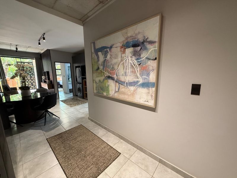 A well-maintained hallway featuring tiled flooring and an exposed concrete ceiling, leading into an open-plan living and kitchen area.