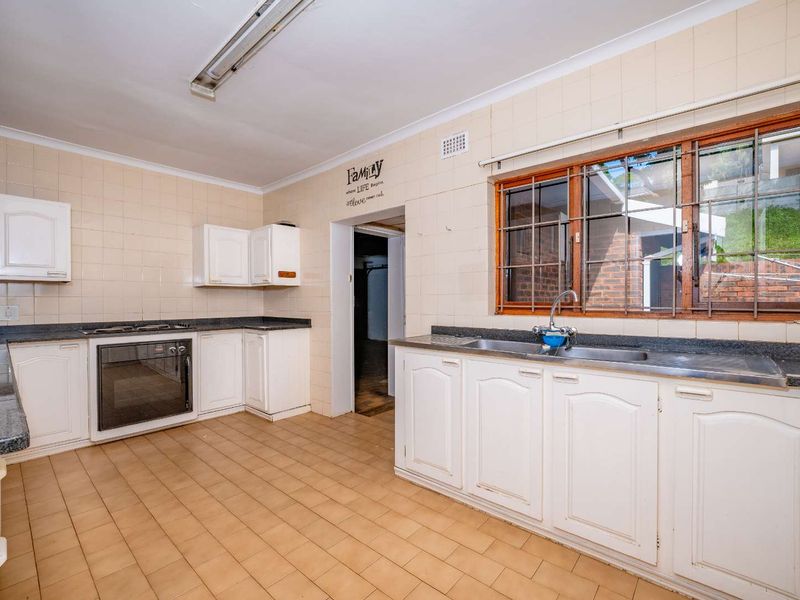 A spacious, dated kitchen featuring white cabinetry, tiled splashbacks, and built-in appliances, offering a blank canvas for modern renovation.