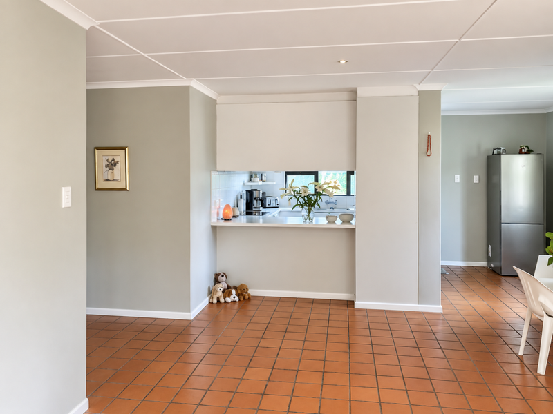 Open plan living area featuring terracotta tiled flooring, coved cornicing, and a convenient kitchen pass-through window connecting to the kitchen space.