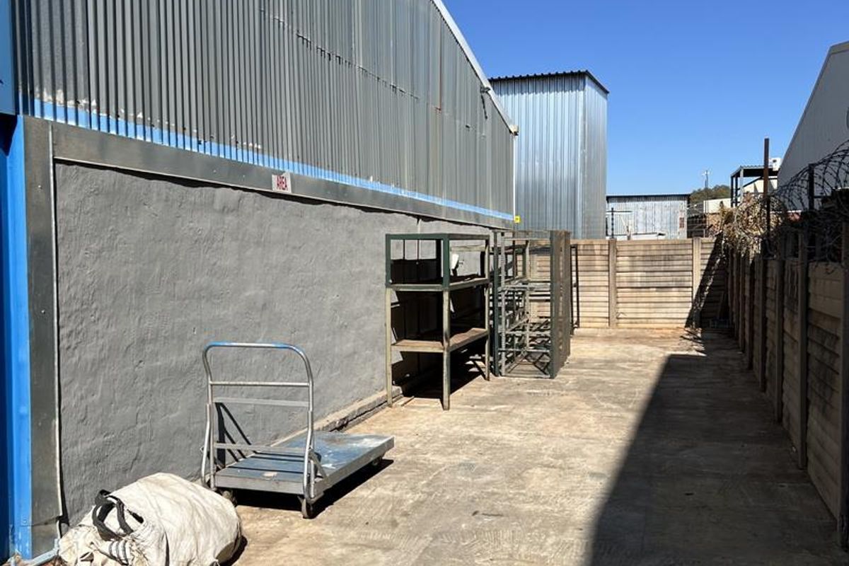 Exterior side yard area featuring concrete paving, corrugated metal wall cladding, and perimeter security fencing with razor wire.