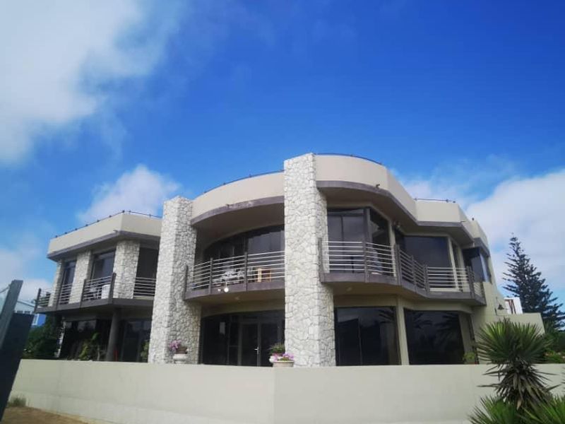 A modern multi-story residence featuring stone-clad pillars, expansive glass sliding doors, and upper-level balconies with stainless steel railings.