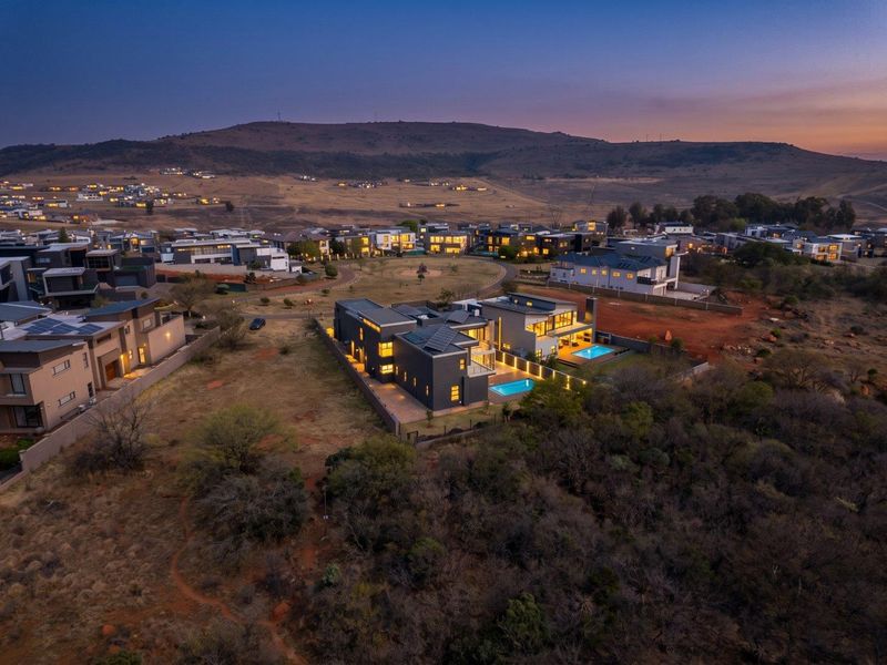 Aerial view of a modern luxury residence at dusk, featuring a swimming pool, solar panels, and expansive views of the surrounding estate landscape.