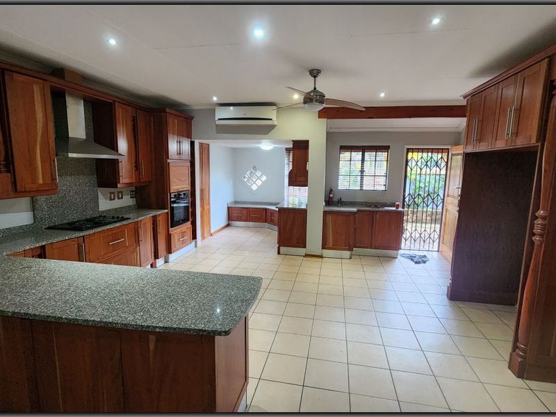 Spacious kitchen featuring extensive wooden cabinetry, granite countertops, built-in appliances, tiled flooring, and direct access to the exterior via a security gate.