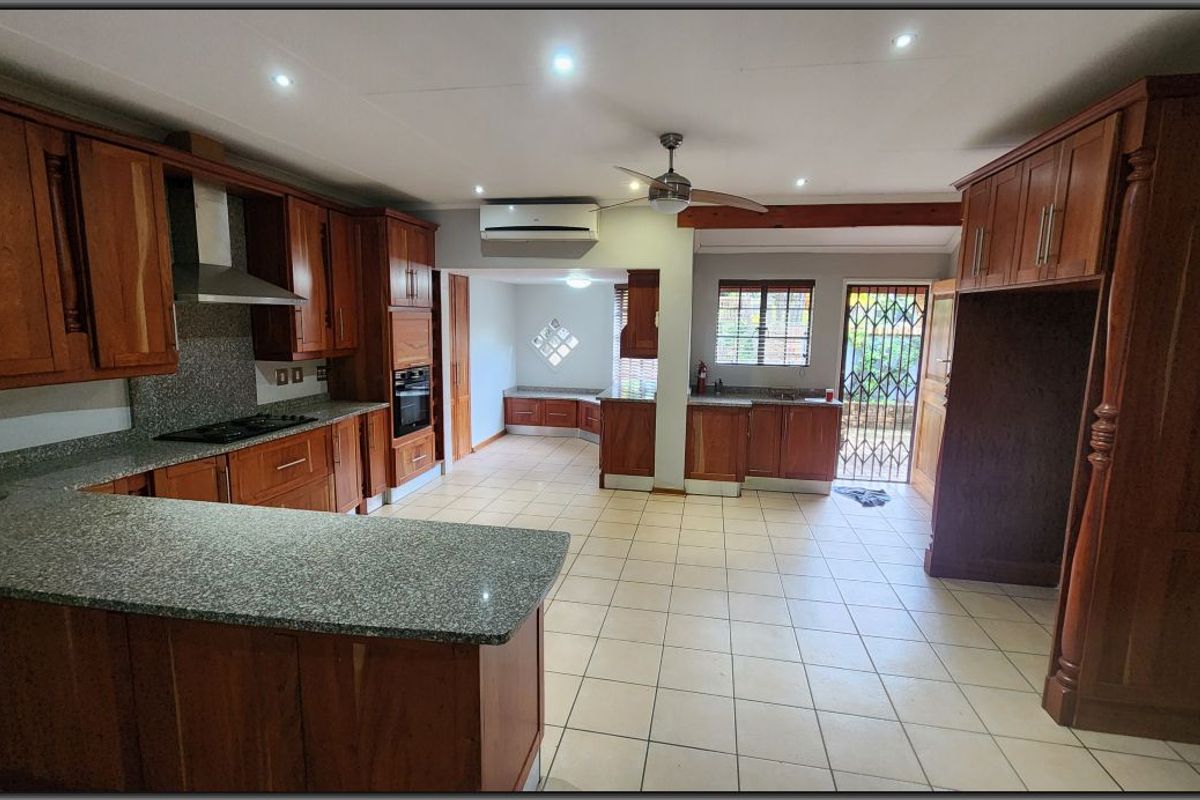 Spacious kitchen featuring extensive wooden cabinetry, granite countertops, built-in appliances, tiled flooring, and direct access to the exterior via a security gate.