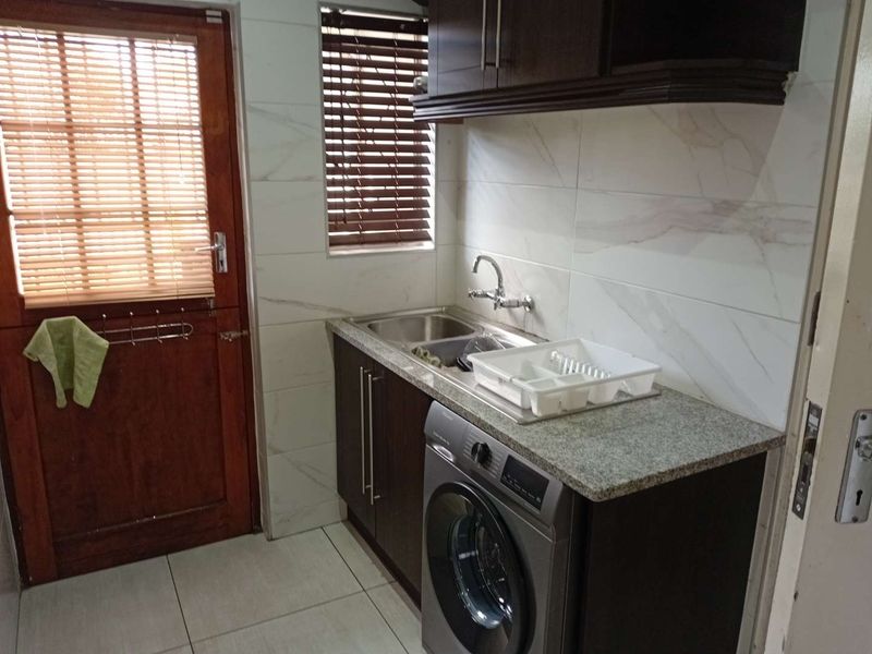 A functional laundry area featuring built-in dark cabinetry, granite countertops, a stainless steel sink, and tiled finishes with direct exterior access.