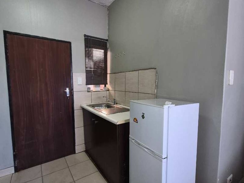A compact kitchen area featuring a single sink unit, tiled backsplash, and tiled flooring, requiring cosmetic updates to improve its overall condition.