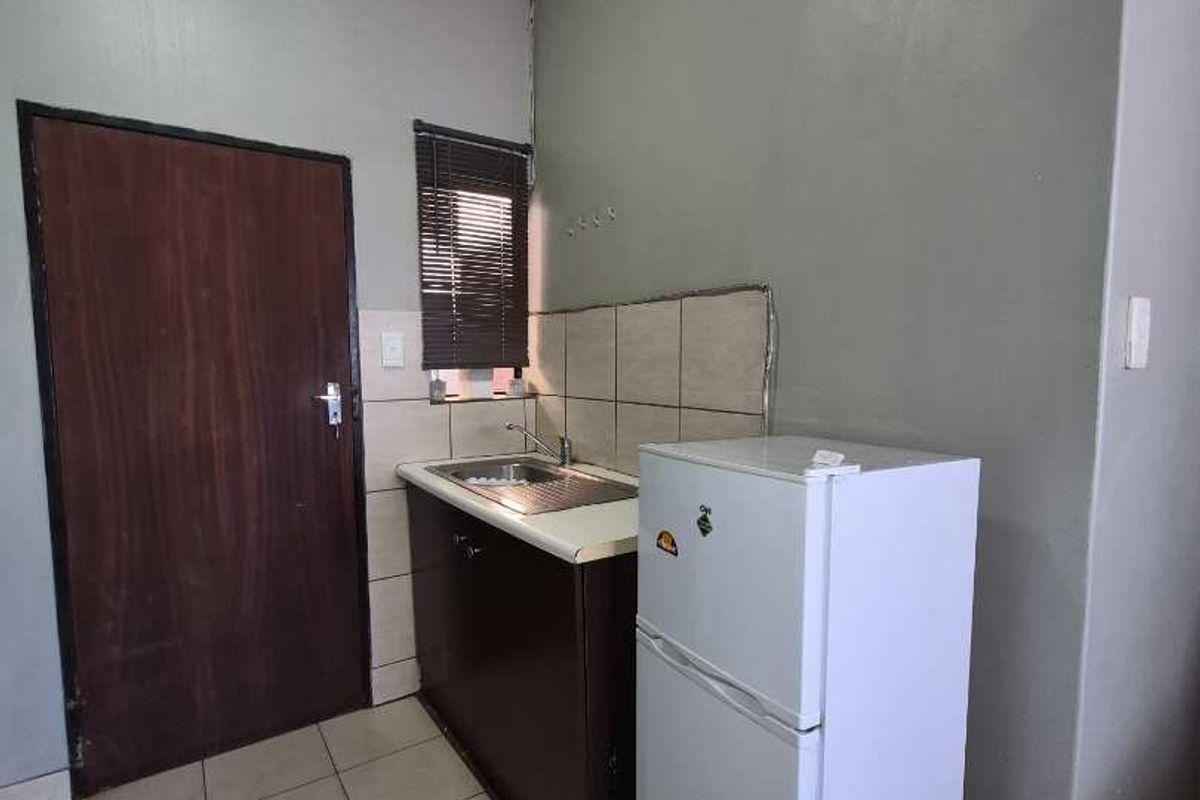 A compact kitchen area featuring a single sink unit, tiled backsplash, and tiled flooring, requiring cosmetic updates to improve its overall condition.