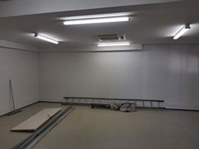 An empty, open-plan office space featuring neutral walls, fluorescent lighting, and a recessed ceiling air conditioning unit.