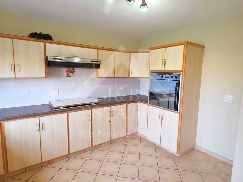 A functional kitchen featuring light wood-tone cabinetry, built-in oven, extractor fan, and tiled flooring, offering a clean and practical workspace.