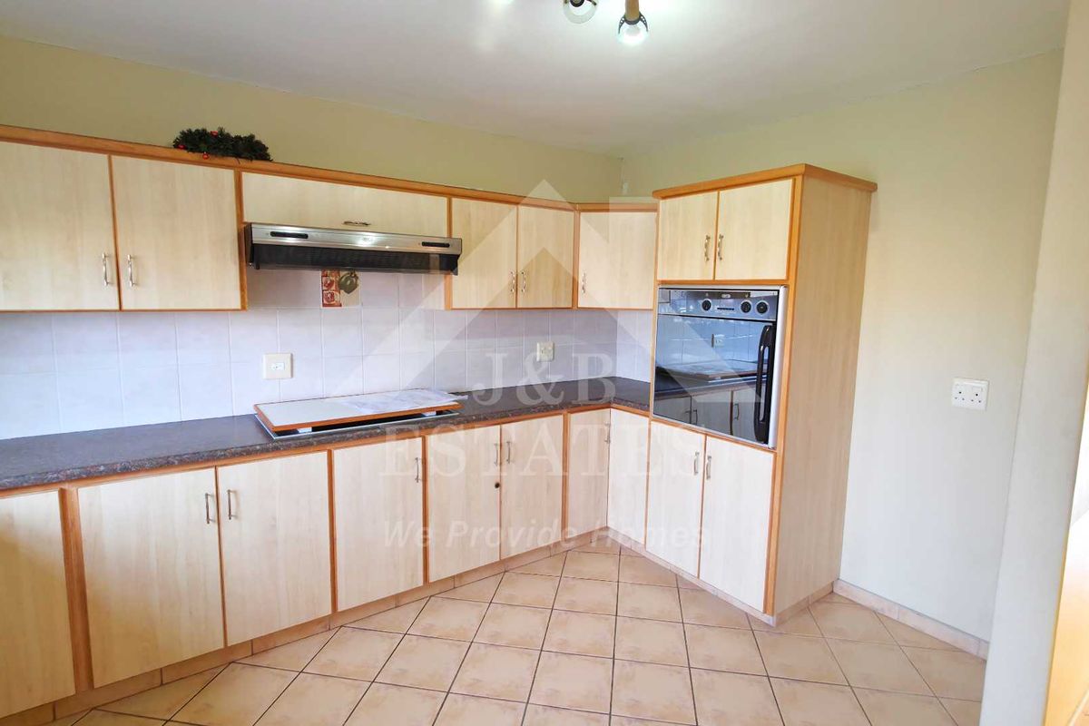 A functional kitchen featuring light wood-tone cabinetry, built-in oven, extractor fan, and tiled flooring, offering a clean and practical workspace.