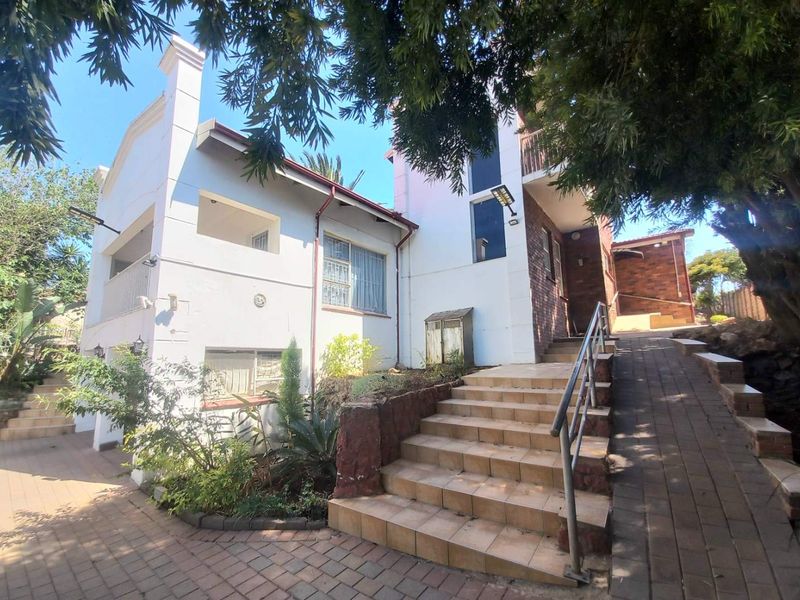 Front exterior view of the property featuring a paved driveway, tiled staircase with metal handrails, and a multi-level facade with balcony access.