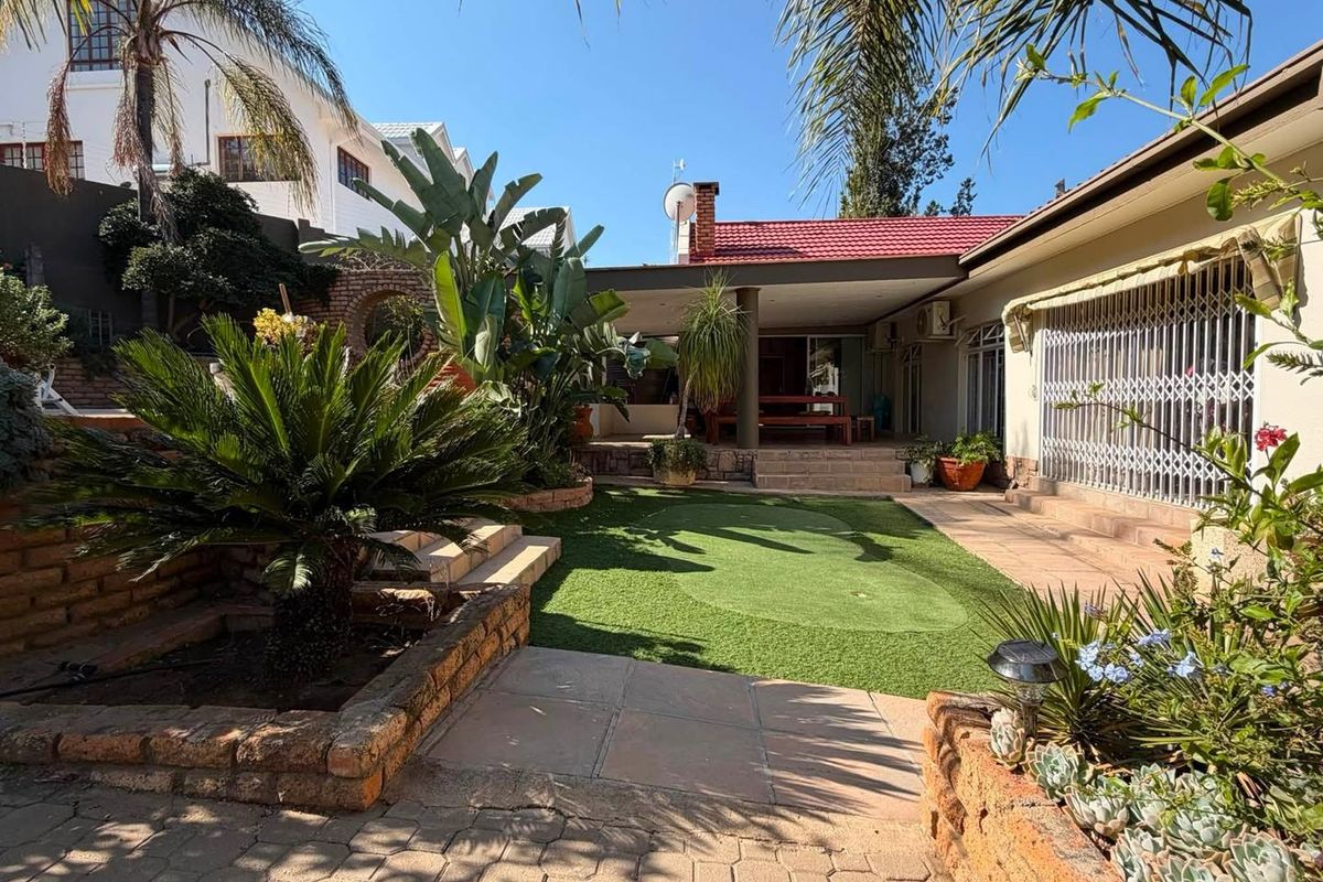 A well-maintained rear garden featuring a covered patio, artificial lawn, brick retaining walls, and paved terrace areas, providing a functional outdoor entertainment space.