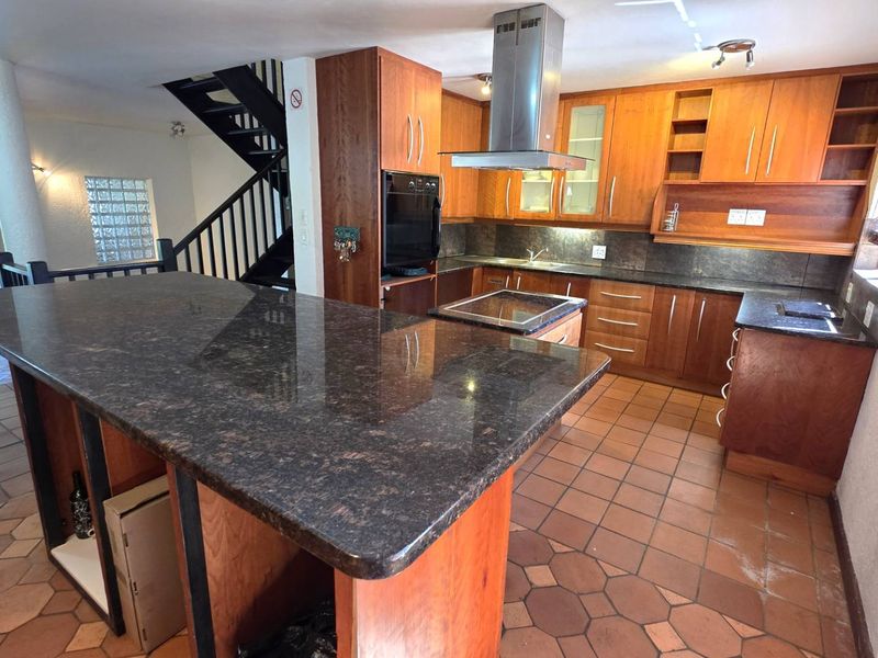 Spacious kitchen featuring granite countertops, wooden cabinetry, built-in oven, and extractor fan, with an open-plan layout leading to a staircase.