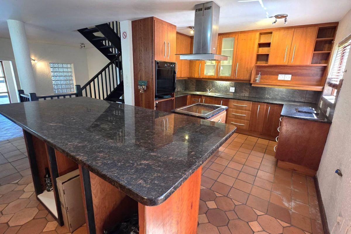 Spacious kitchen featuring granite countertops, wooden cabinetry, built-in oven, and extractor fan, with an open-plan layout leading to a staircase.