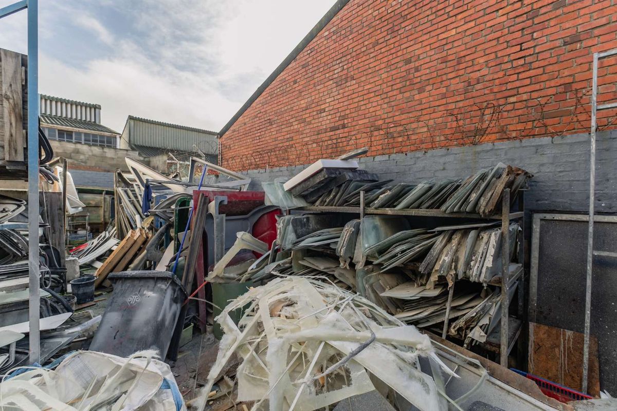 An exterior rear industrial yard area featuring a brick perimeter wall with security wire and significant accumulation of industrial materials and debris.