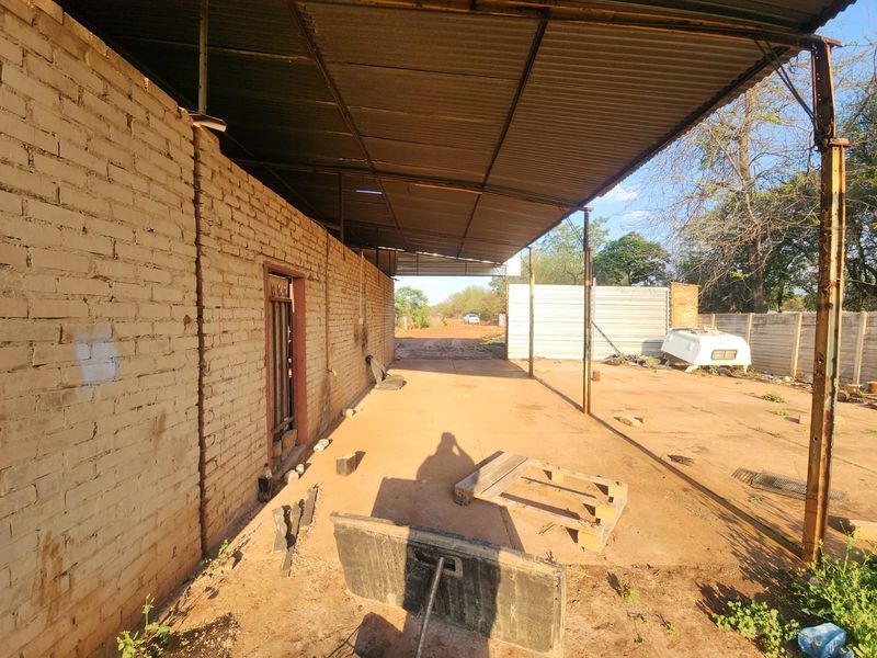 An expansive outdoor utility area featuring a large corrugated metal roof structure supported by metal columns, adjacent to an exposed brick wall.