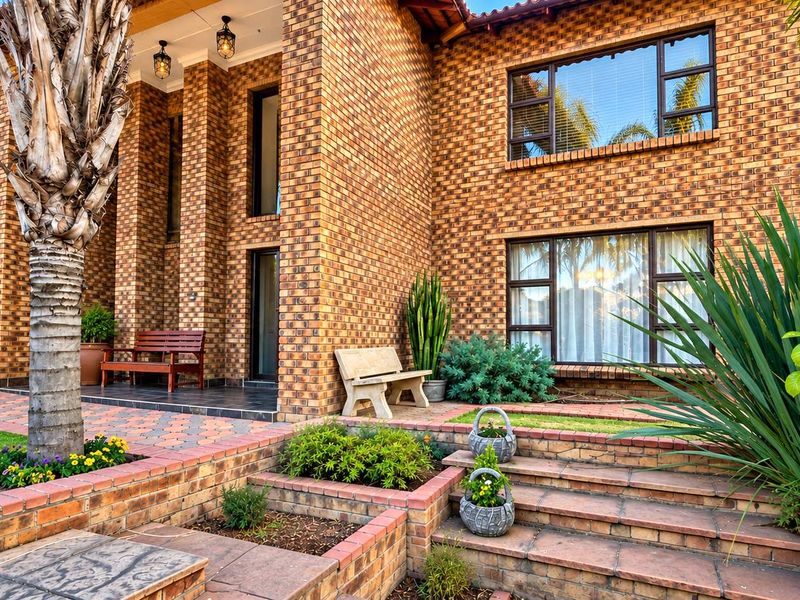 A well-maintained double-storey face brick home featuring a paved driveway, tiered garden beds with brick retaining walls, and a secure garage.