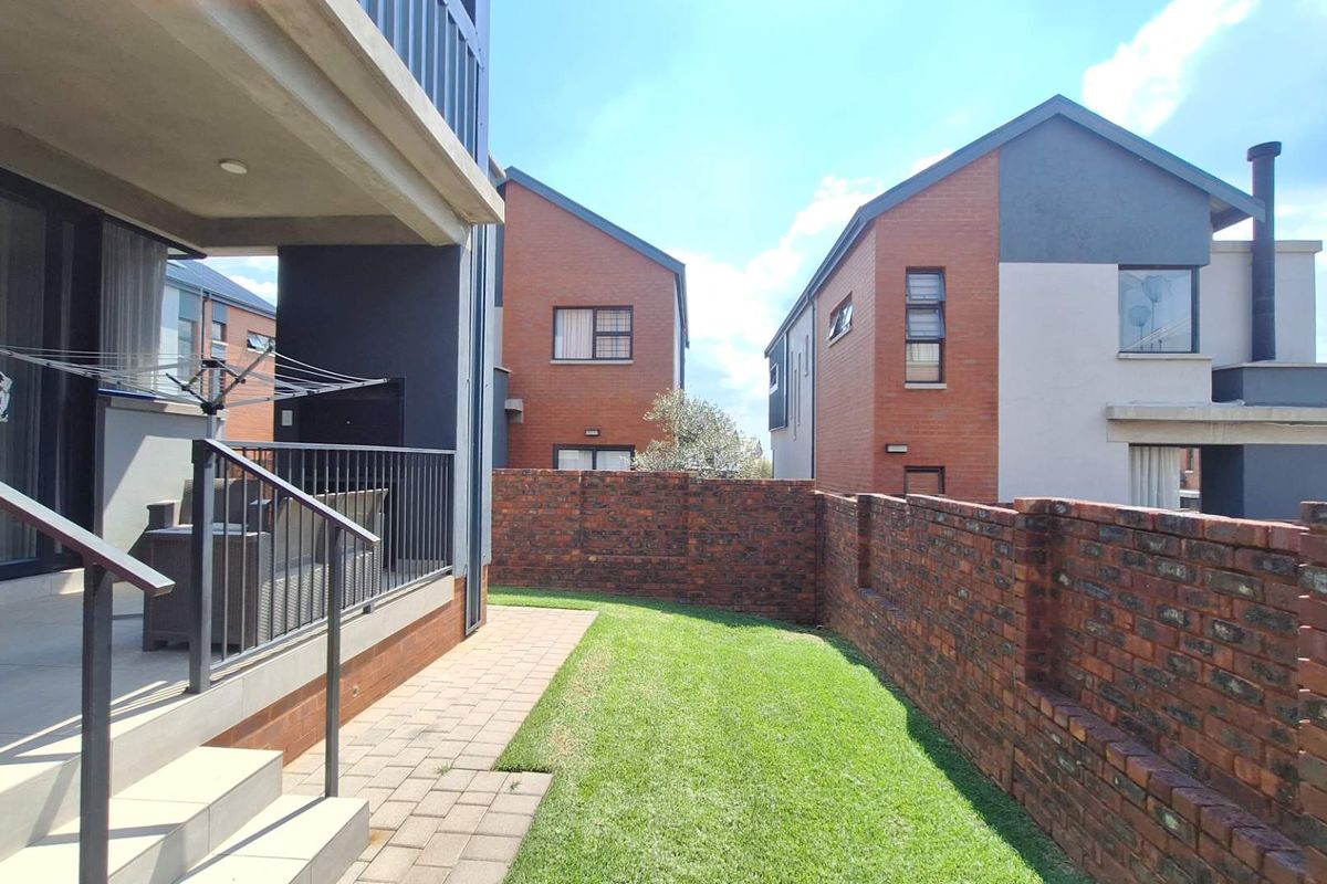 A private rear garden featuring a well-maintained lawn, a paved patio area, and a brick boundary wall, adjacent to a covered patio.