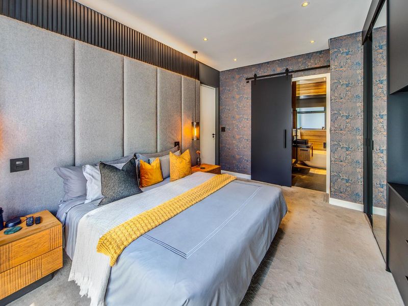 Modern bedroom featuring custom upholstered wall paneling, a sleek sliding barn door leading to an en-suite, and integrated wardrobe storage.