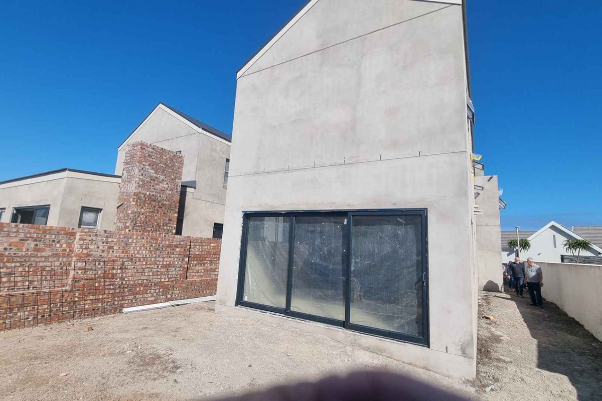 Rear view of a house under construction featuring large sliding glass doors, exposed brick boundary walls, and unfinished exterior plastering.