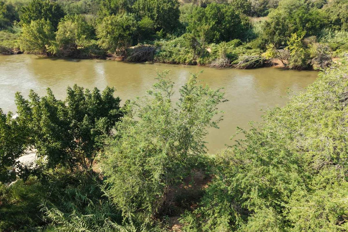 A scenic elevated view of a natural river flowing through a lush, tree-lined landscape, highlighting the property's tranquil waterfront setting.