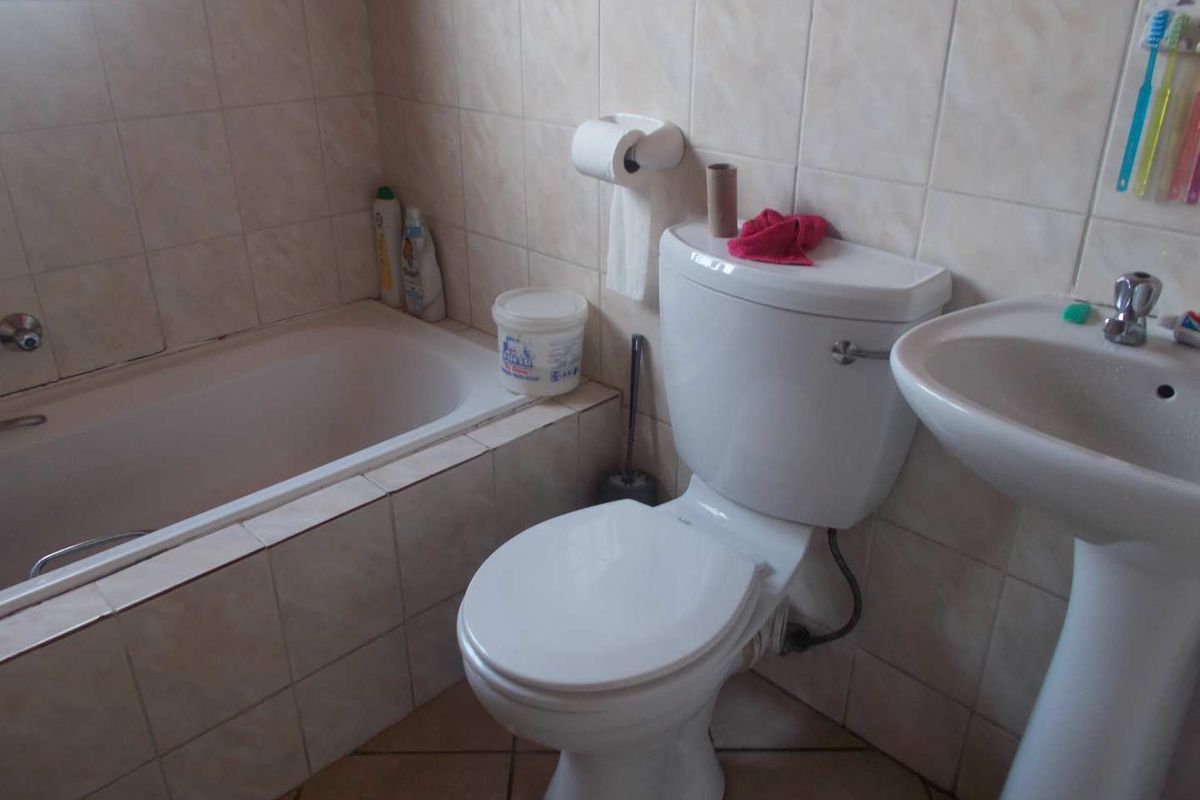 A functional bathroom featuring a bathtub, pedestal basin, and toilet with neutral ceramic wall and floor tiling.