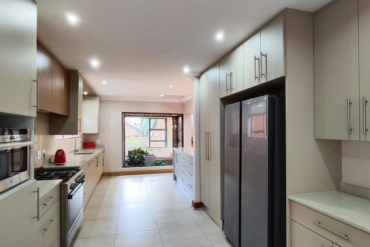 Modern galley-style kitchen featuring sleek cabinetry, integrated oven, gas hob, and tiled flooring, leading to a bright windowed area.
