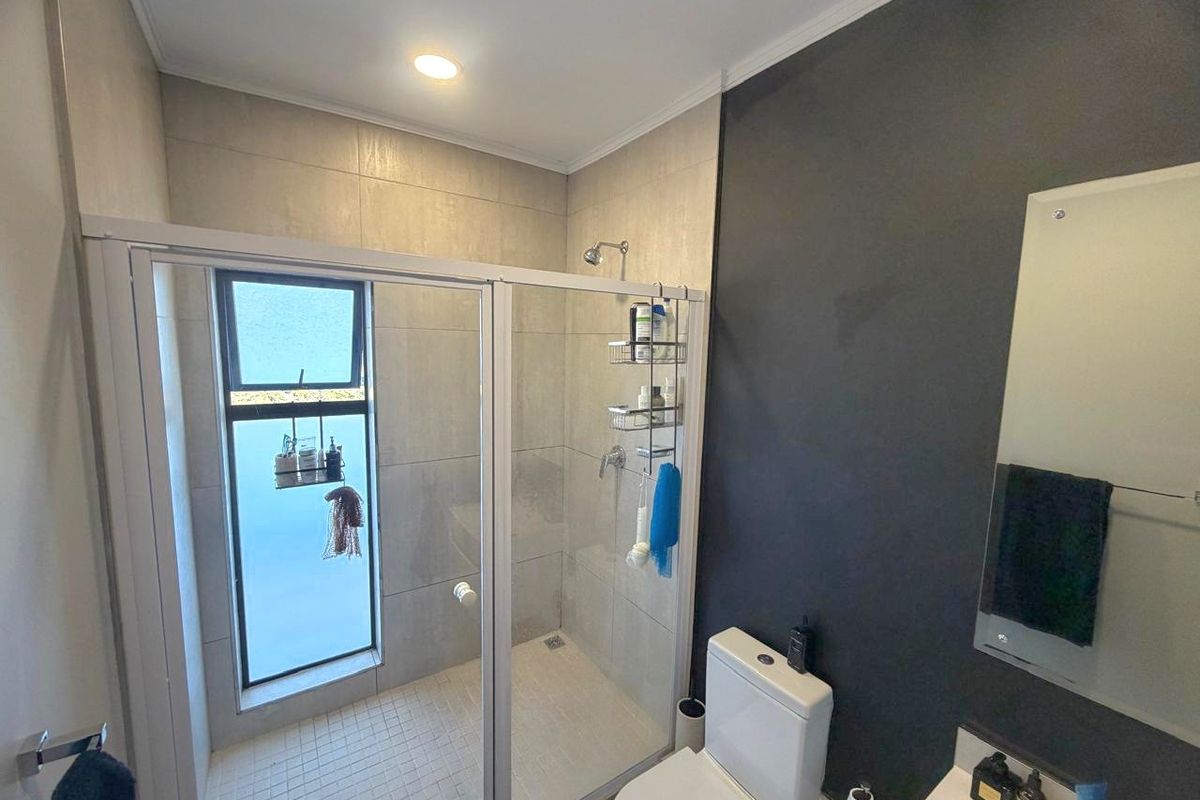 A modern bathroom featuring a glass-enclosed shower, tiled walls, a toilet, and a vanity basin with a wall-mounted mirror.