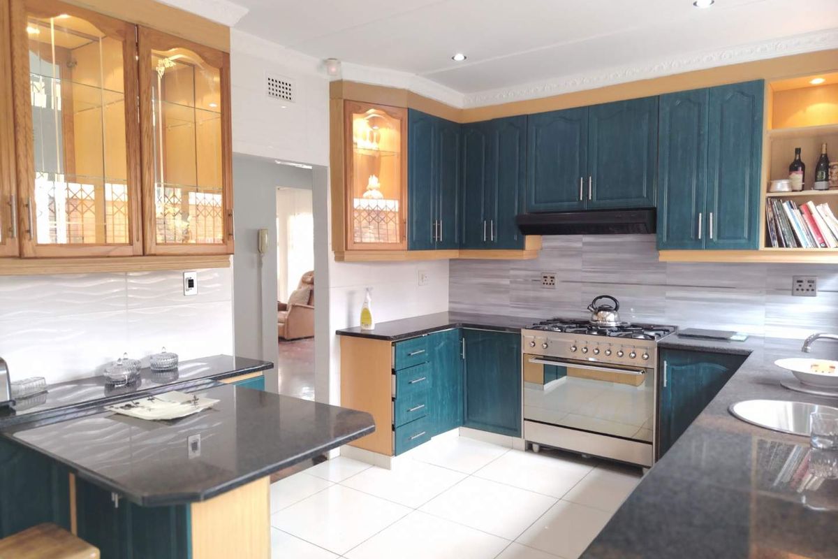 A well-maintained kitchen featuring dark blue cabinetry, granite countertops, a gas stove with extractor fan, and tiled flooring.