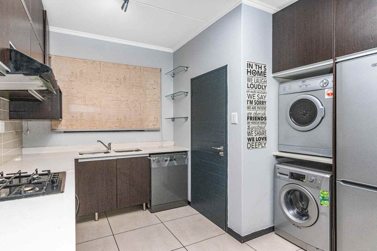 A functional kitchen and laundry area featuring dark cabinetry, a gas hob, integrated dishwasher, and stacked laundry appliances.