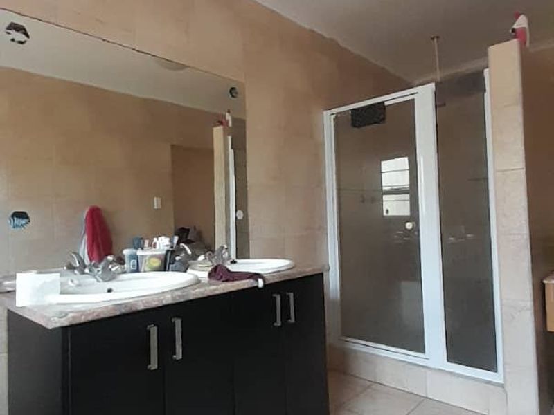 A functional bathroom featuring a double vanity with dark cabinetry, a glass-enclosed shower, and neutral wall and floor tiling.