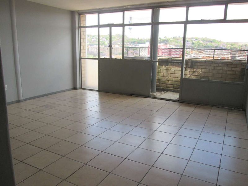 An empty, open-plan living area featuring tiled flooring and large windows that provide natural light and access to an outdoor balcony space.