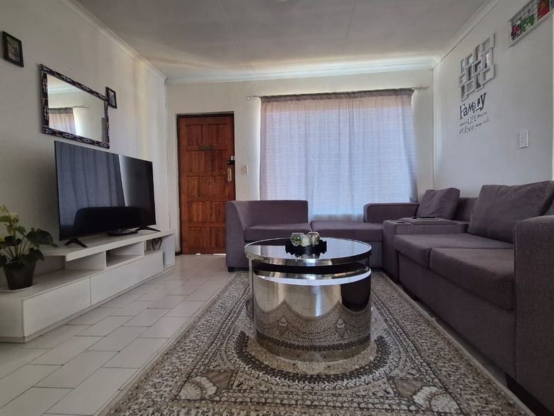 A comfortable living room featuring tiled flooring, a timber entrance door, and a sliding door providing access to the outdoor area.