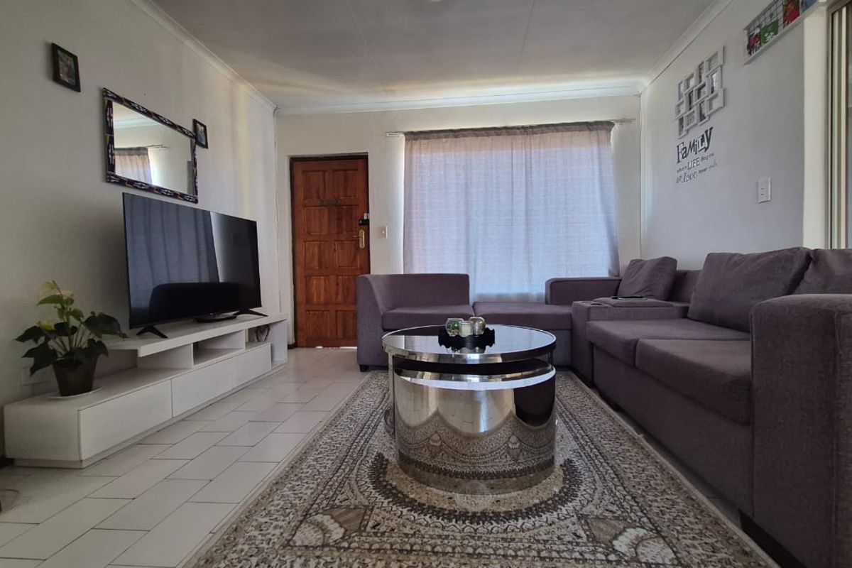 A comfortable living room featuring tiled flooring, a timber entrance door, and a sliding door providing access to the outdoor area.