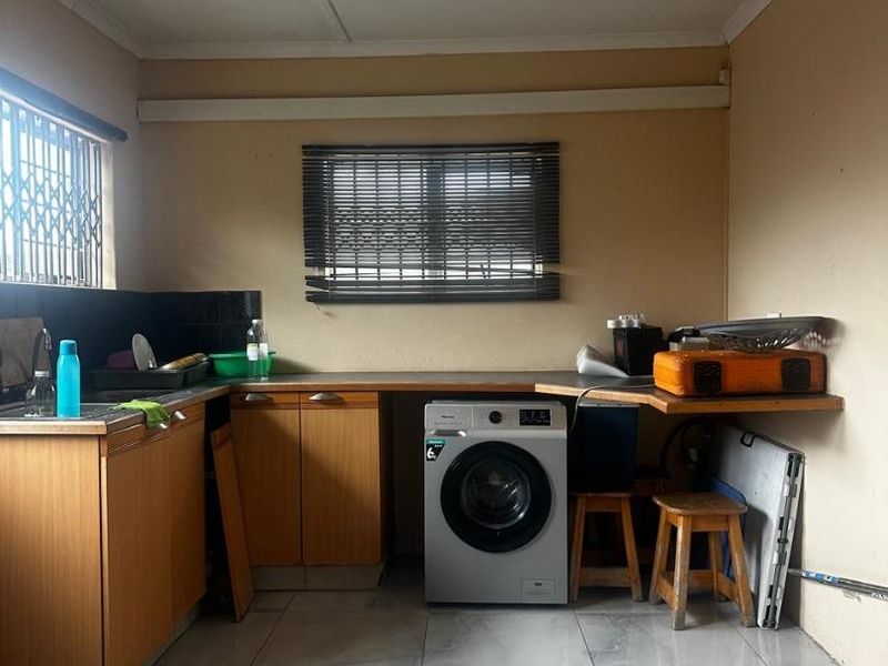 Functional laundry area featuring tiled flooring, built-in cabinetry with laminate countertops, and a stainless steel sink.