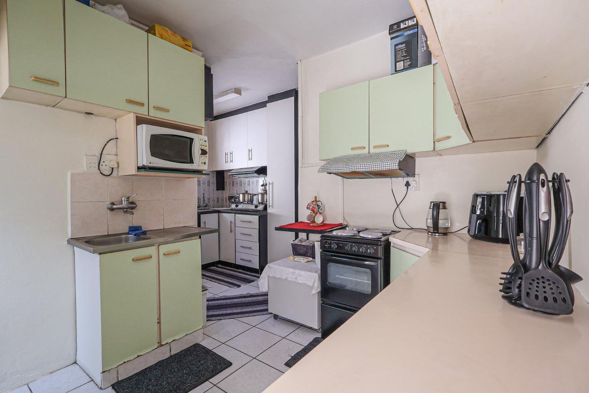 A functional kitchen featuring light green cabinetry, a freestanding stove with extractor fan, and tiled flooring, offering a practical layout for daily meal preparation.