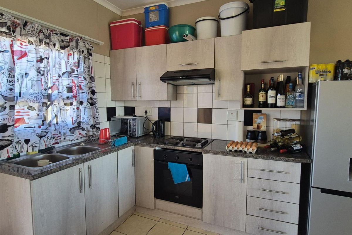 A functional kitchen featuring light wood-grain cabinetry, a built-in oven, gas hob, extractor fan, and a double-basin stainless steel sink with tiled splashbacks.