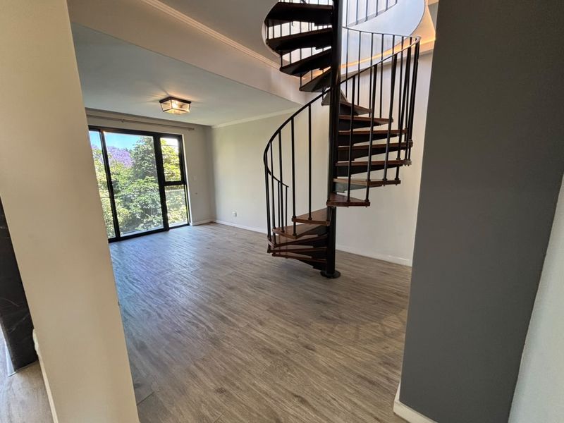 Spacious living area featuring a striking spiral staircase, modern laminate flooring, and large sliding glass doors that provide ample natural light.
