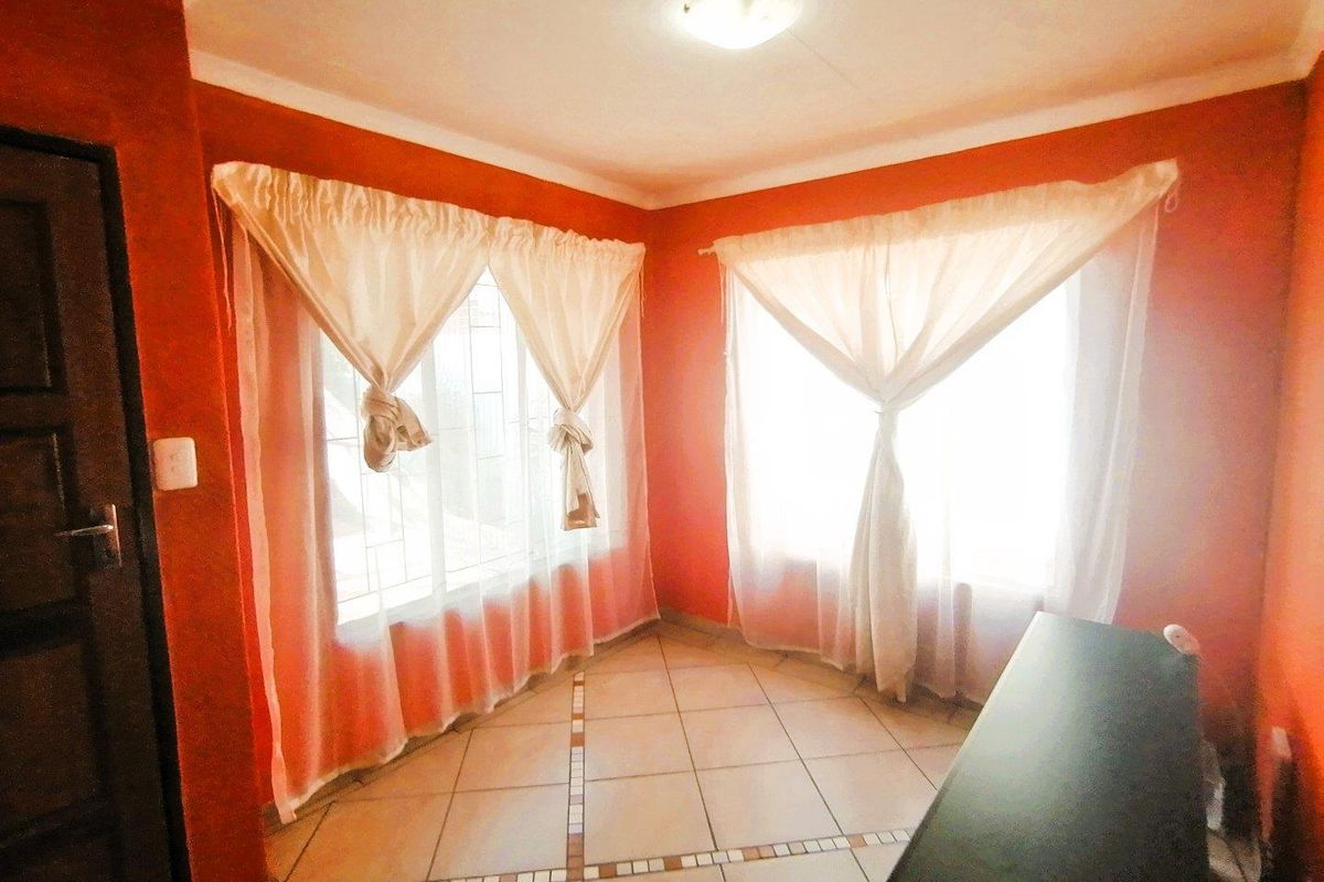 A bright living room featuring tiled flooring, large windows with curtains, and bold wall paint, offering a functional space for relaxation.