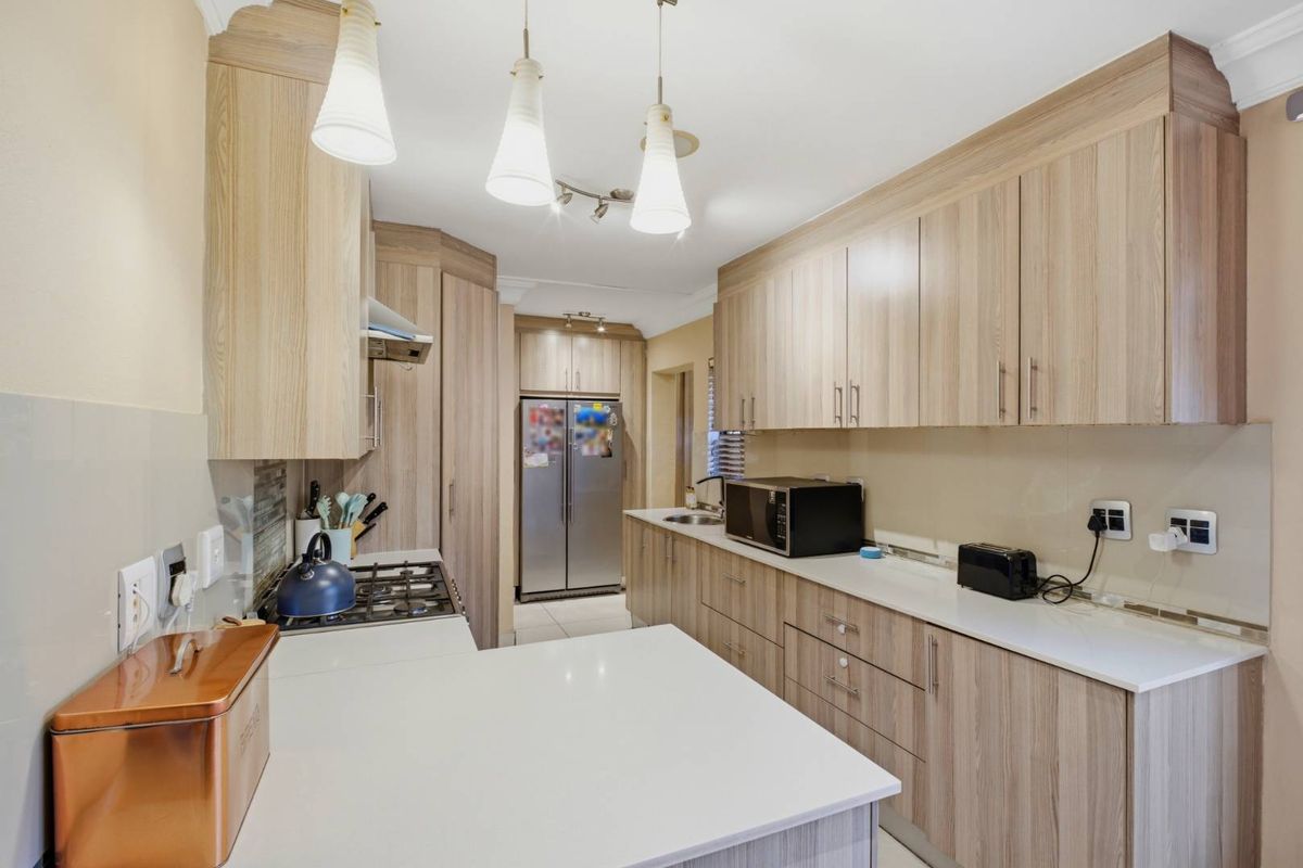 A functional kitchen featuring light wood-grain cabinetry, stone-look countertops, a built-in gas hob, and an integrated extractor fan.